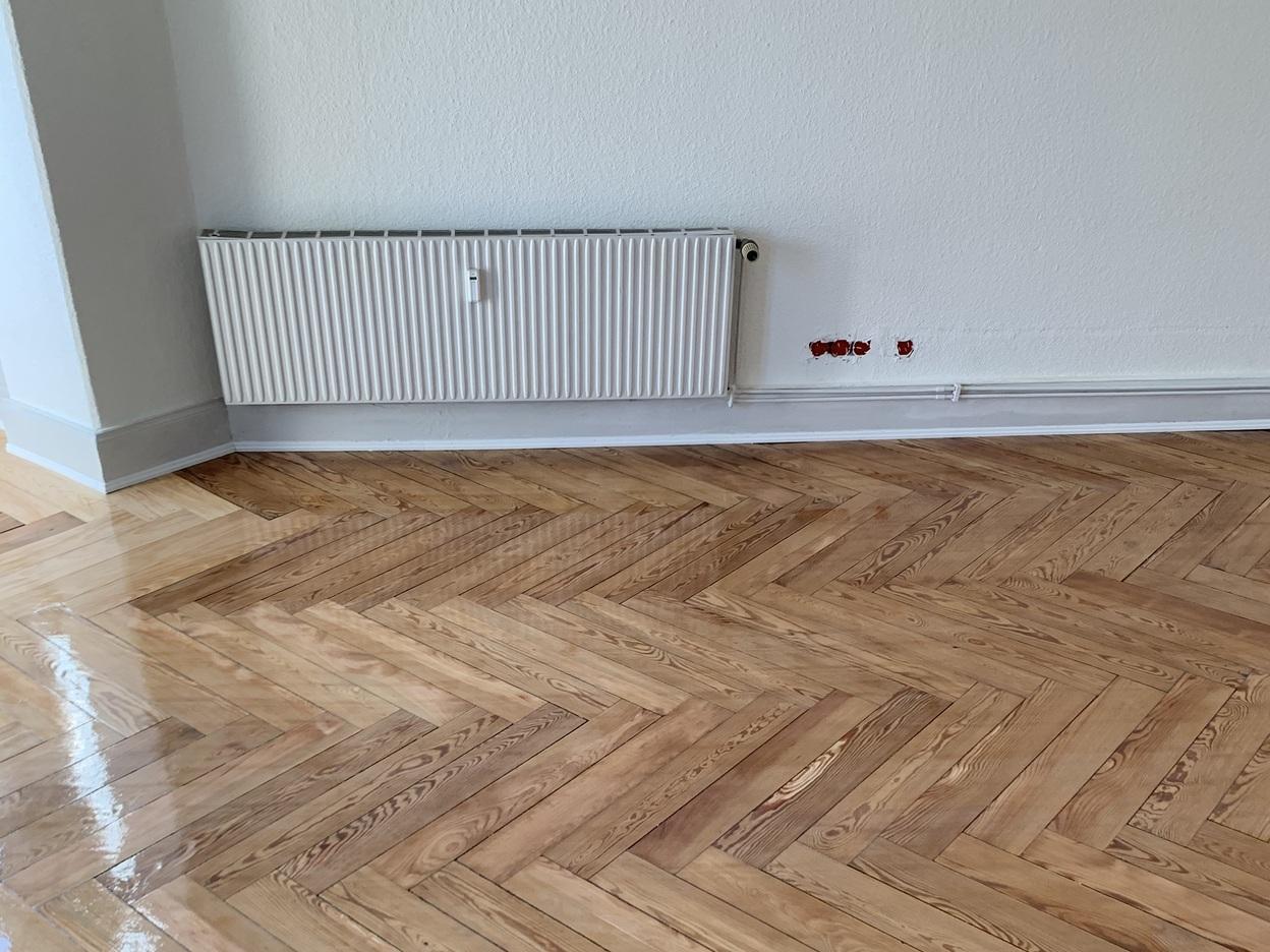 Bild zeigt einen detailreichen Fischgrät-Parkettboden mit glänzender Oberfläche in einem leeren Raum