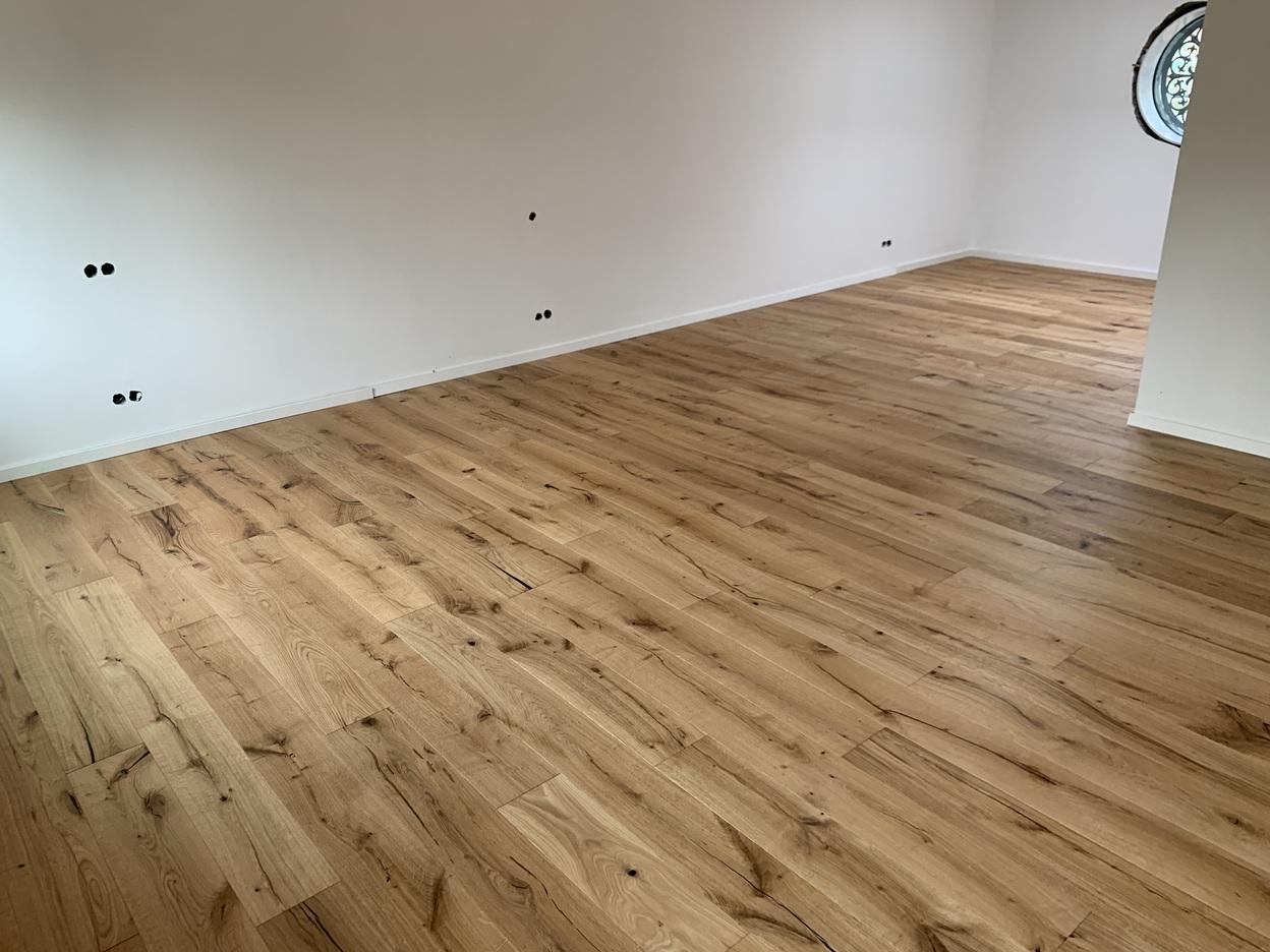 Ein naturbelassener Holzboden mit einzigartiger Maserung in einem großen, leeren Raum. Die individuelle Verlegung betont das rustikale Design. Individueller Boden.