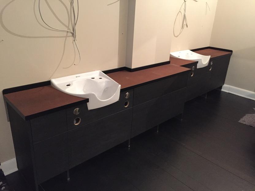 Maßgefertigte Waschtische in einem Friseursalon Zwei maßgefertigte Waschtische mit weißen Becken und dunklen Unterschränken befinden sich im Aufbau in einem Friseursalon. Kabel hängen bereit für die Installation. Friseursalon.