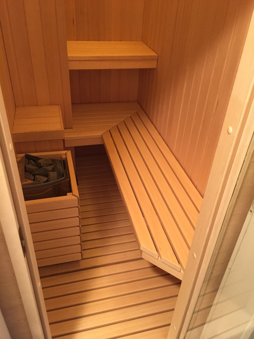Bild zeigt das Innere einer Sauna mit honigfarbenen Holzbänken und vertikalen Holzpaneelen an den Wänden.