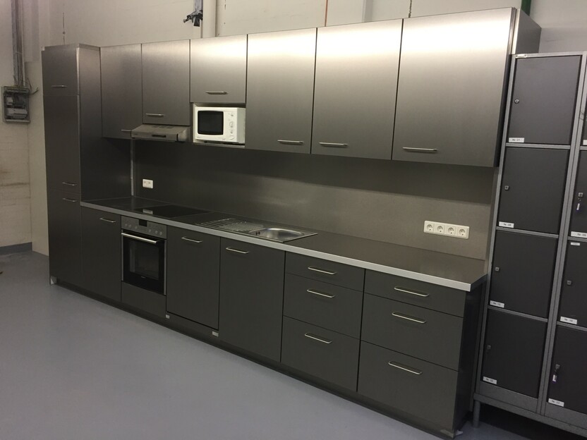 Bild einer modernen Küchenzeile mit dunkelgrauen Schränken und Edelstahleinrichtungen. Die Küche ist ausgestattet mit einem Einbauherd, einer Mikrowelle und einer Spüle.