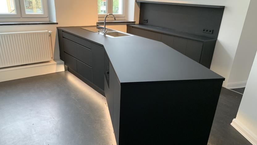 Das Bild zeigt eine moderne Küche mit einer großen schwarzen Insel in der Mitte. Die Arbeitsplatte der Insel ist ebenso schwarz und bildet einen nahtlosen Übergang zu den Schränken.