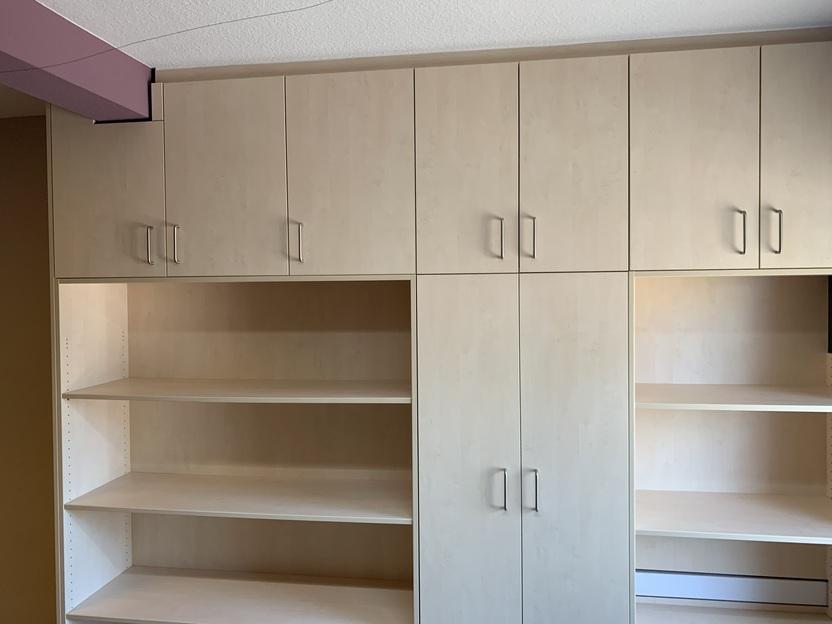 Ein ma&szlig;gefertigter Einbauschrank aus hellem Holz mit hohen Schrankt&uuml;ren und offenen Regalf&auml;chern, die zus&auml;tzlichen Stauraum bieten. Der Schrank ist perfekt in den Raum integriert. Schrank nach Ma&szlig;.