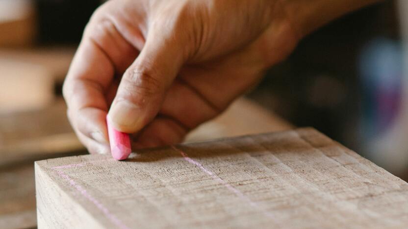 Eine Hand zeichnet mit Kreide präzise Markierungen auf ein Holzstück, um Möbel nach Maß anzufertigen. Das Bild zeigt den ersten Schritt der Holzbearbeitung im Möbelbau.