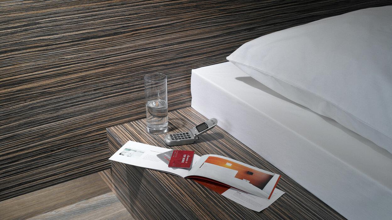 Detailaufnahme von Bettumrandung in dunklem Holz mit Ablagemöglichkeit